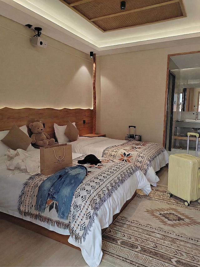 保持地毯、小熊抱枕、牛仔外套和浅黄色行李箱不变，在床上添加一个购物袋，保持房间整体布局和装修风格不变