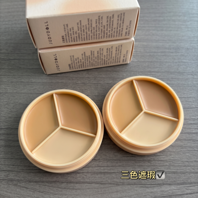将图二的三色修容膏产品，按照图一的构图摆放，生成跟图一一样的实拍主图，摆放视角跟图一保持一致，产品数量对标图一为两个产品，使用图一相同的灰色木纹实拍背景，保持产品本身的质感和清晰度，突出产品材质，去除预览效果