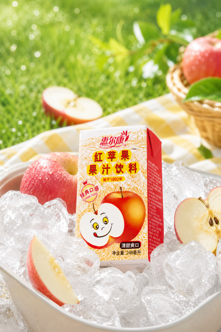 惠尔康红苹果果汁饮料电商海报，保持参考图清爽夏日冰爽户外的风格，将包装盒放在冰块中，搭配新鲜苹果切片，背景为绿色户外草地，构图与参考图不同，突出产品清凉清甜的特点预览效果