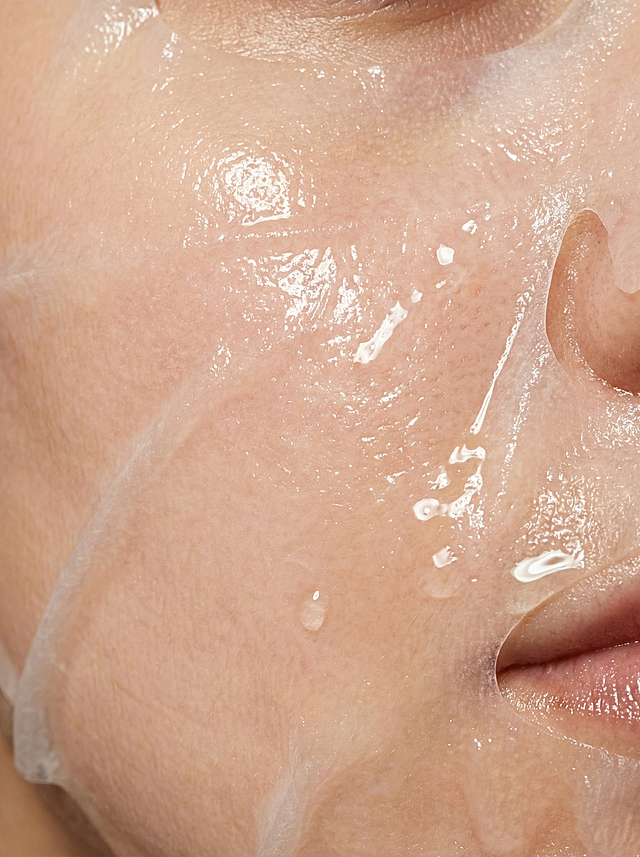 特写镜头，一张贴在人体肌肤上的补水膜布，膜布充满水润光泽，质感细腻通透，水润透亮带有精华液的湿滑反光，细节清晰，产品摄影质感，高清写实