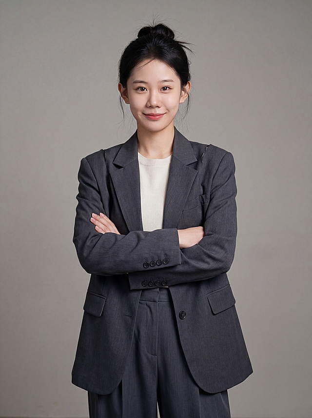 参考图中保留人物脸型、发型、年龄等特征生成职场形象照,标准焦段50mm,f/4光圈(f/2.8-f/4区间),平视视角(镜头与人物视线齐平);人物占画面70%,人物居中(居中构图),位于画面中心,为视觉聚焦点,入境范围头部及以下至臀部下方10cm(半身像);左右留少量背景空间;头部与画面顶部保留5%空间;头部发型完整,头肩比例协调,人物结构准确;发质微微柔顺，微微蓬松。身穿设计师款小众解构剪裁深灰色西装外套;内搭简约米白色针织衫;下装深灰色垂感阔腿西装裤;着装正式干练;前卫自信,灵感充沛,艺术格调,张扬有态度;身形匀称,姿态端正,身体挺拔。呈自然站姿+双手抱胸，肢体放松且自信;佩戴精致配饰,简约微微中性灰色纯色背景(呈现均匀柔和质感),背景光线均匀柔和,强化色彩对比的高级感。极简干净;画质超高分辨率、细节清晰,现代精致感风格;肤质精细化处理;眼神直视镜头,目光坚定且澄澈,表情自然。嘴角上扬;清透自然裸妆(轻薄底妆+淡唇妆)妆感轻薄轻透裸肌感,通透感肤质,肤质自然细腻,肤色健康均匀,雾面柔光裸肌感,保留真实皮肤细节｡正面柔光补光,4800K中性光,面部光比1:1.5,色调明亮｡中近景写实摄影,对焦清晰,高清保留皮肤细节｡分辨率4K,去除人物之外的所有元素。严格按照图片内容生成。画面比例3:4