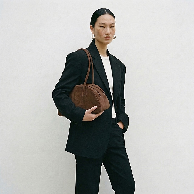 将第二张图中模特背的包替换为第一张图里的棕色麂皮双拉链长肩带手提包，保持模特姿态和画面整体风格不变，光影与环境融合自然