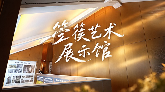 基于这张箜篌艺术展示馆的室内照片，设计16:9的视频封面。在画面正中间添加大号白色文字“箜篌艺术展示馆”，标题居中，分两行展示（第一行“箜篌艺术”，第二行“展示馆”）。文字采用随性自然的手写风格，充满灵动与艺术感，笔画线条流畅且富有变化，粗细不一，笔触灵动洒脱，部分笔画较为纤细轻盈，似信手拈来，给人轻松洒脱之感，仿佛是作者在自然状态下快速书写而成，传递出自由、洒脱且富有诗意的氛围。白字具有设计感，文字要大，位于画面正中央。背景保留原展馆的空间氛围，适当增强艺术感和光影层次，整体画面和谐美观。
