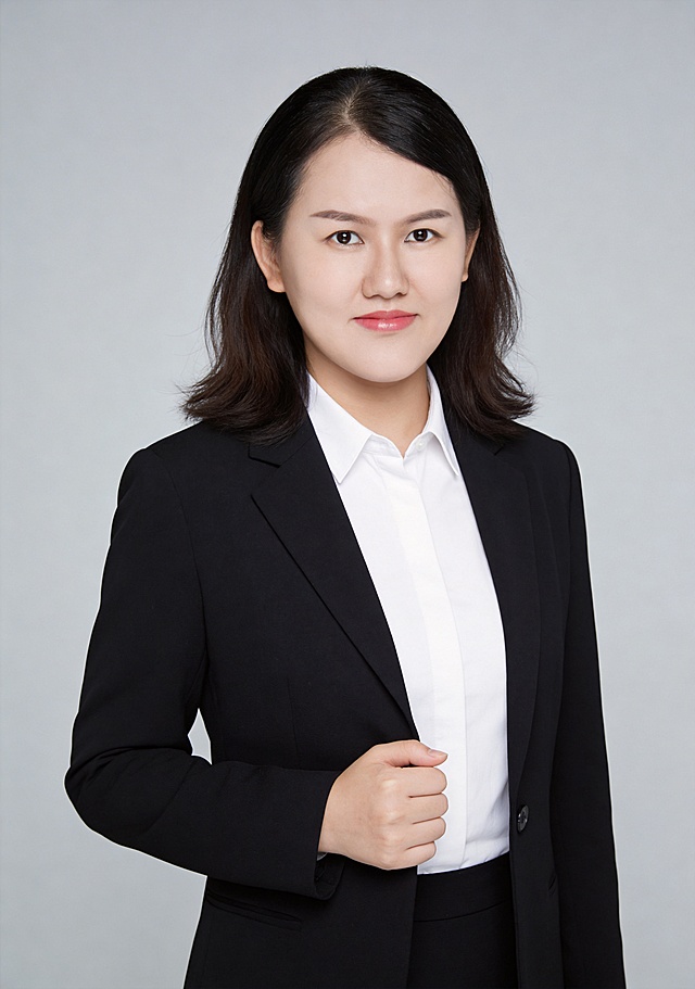 参考图中保留人物脸型、发型、年龄等特征生成职场形象照,标准焦段50mm,f/4光圈(f/2.8-f/4区间),平视视角(镜头与人物视线齐平);人物占画面70%,人物居中(居中构图),位于画面中心,为视觉聚焦点,入境范围头部及以下至臀部下方10cm(半身像);左右留少量背景空间;头部与画面顶部保留5%空间;头部发型完整,头肩比例协调,人物结构准确;发质微微柔顺，微微蓬松。身穿白色高支精梳棉衬衫,(翻领设计,面料呈细腻微微哑光质感);下装与上衣同材质;着装正式干练;专业稳重;身形匀称,姿态端正,身体挺拔。呈自然站姿，右手轻握西装前襟，肢体放松且自信;简约微微中度灰色纯色背景(呈现均匀柔和质感),背景光线均匀柔和,强化色彩对比的高级感。极简干净;32k画质超高分辨率、细节清晰,现代精致感风格;肤质精细化处理;眼神直视镜头,目光坚定且澄澈,表情自然。嘴角上扬;韩式美颜磨精致妆容,自然裸妆(清透底妆+淡色唇妆),妆感轻薄,肤质精细化处理;白皙清透肤质透亮,微微柔光提亮,细腻无瑕,通透高级感干净清透肤质,肤色均匀,肌肤柔光美白细腻,自然提亮,光影柔和通透水光肌,肤质细腻平滑干净哑光肤质,无油光无暗沉;干净肤色,健康肤色,无蜡黄,无暗沉,无黄皮,肤质细腻,高清皮肤细节;微微修饰脸型,肤质哑光细腻,面部雾面柔光,轻透裸肌感,真实毛孔纹理,杰作,最佳画质,超高细节,写实摄影,中近景人像,面部清晰,五官精致,皮肤细腻通透,白皙清透皮肤,干净肤色,柔光,正面补光,面部光线均匀明亮,无浓重阴影,冷色调白平衡,画面干净清新,色调明亮,对焦清晰;分辨率4K,去除人物之外的所有元素。严格按照图片内容生成。