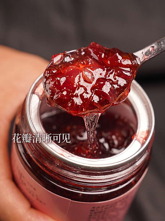 [主图 3] 细节放大展示，突出果酱饱满大颗粒果肉。
[氛围风格] 微距特写，极致食欲感，真实放大产品天然纹理。
[画质] 商业摄影质感、光线柔和通透、产品清晰真实、画面干净高级。
[元素] 保持玫瑰酱质地颜色和输入图片一致，杜绝变形色差。微距特写从罐子舀出的果酱，清晰展示果酱中分布的玫瑰花瓣大颗粒，勺子提拉出自然的果酱拉丝，罐子被手稳稳握住，只展示罐口部分，聚焦果酱主体，商品主体占75%，画面满屏无框。
[光影] 逆光打透果酱，使得每颗花瓣颗粒清晰通透，糖浆晶莹光泽，高光在果酱表面自然流动，纹理细节分毫毕现。
[配色] 浓郁深红果酱为主，暖肤色手和银色罐口做点缀，深色背景衬托主体。
[视角构图] 俯视微距特写，聚焦果酱颗粒，景深较浅突出纹理细节。
[文字版式] 左下角留白，标注文字「花瓣清晰可见」，细体白色带轻投影，不遮挡果酱细节，自然融合。
[比例分辨率] 3:4比例，2k分辨率，文字清晰可辨，超高清。
[负向提示词] 变形，水印，文字错乱，产品图模糊，背景杂乱，颜色失真