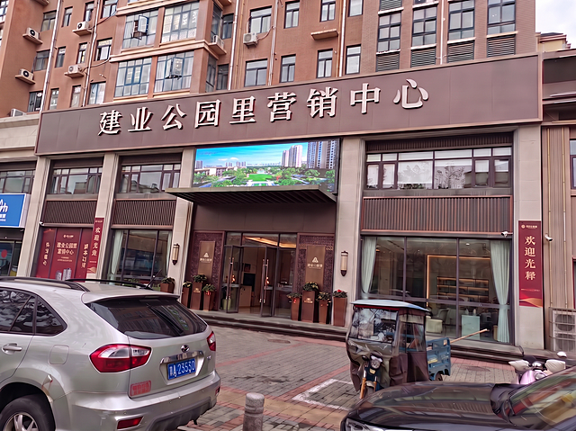 将大屏调整到二楼区域，不可放在三楼，大屏可占用二楼窗户，位置合适协调，保留"建业公园里营销中心"门头文字和一楼原墙体效果，保持白天场景自然真实
