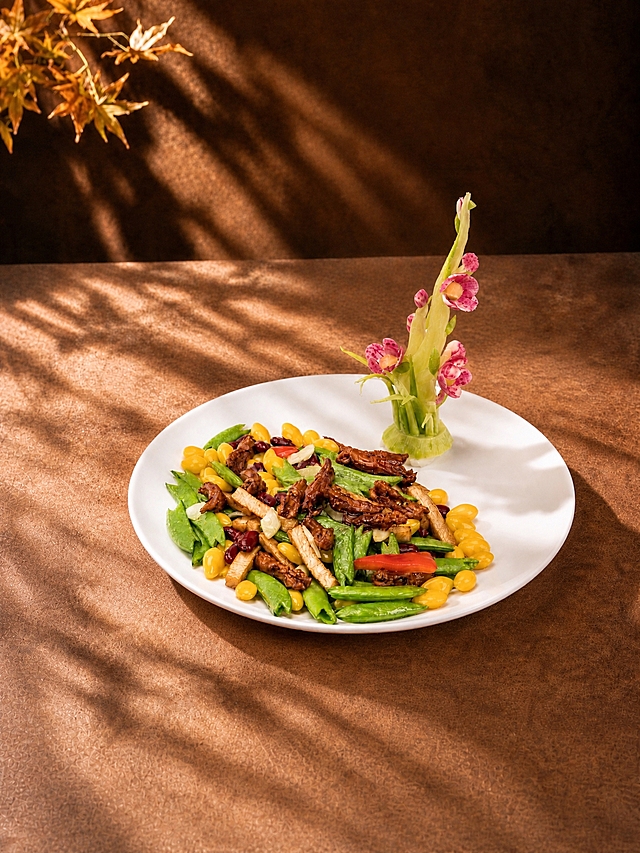 将画面中的银杏蜜豆炒鸭舌菜品（白色圆盘及盘中所有食材、花卉摆盘）整体向上轻微移动一点位置，菜品在画面中的占比保持不变，仅位置上移。背景（暖棕色墙面、左上角枫叶枝叶、枫叶光影、暖棕色桌面、侧逆光氛围）保持不变，桌面下方适当延伸补充，光影和阴影自然跟随调整，整体画面协调自然。保持3:4竖版比例，无文字，写实美食摄影质感不变。