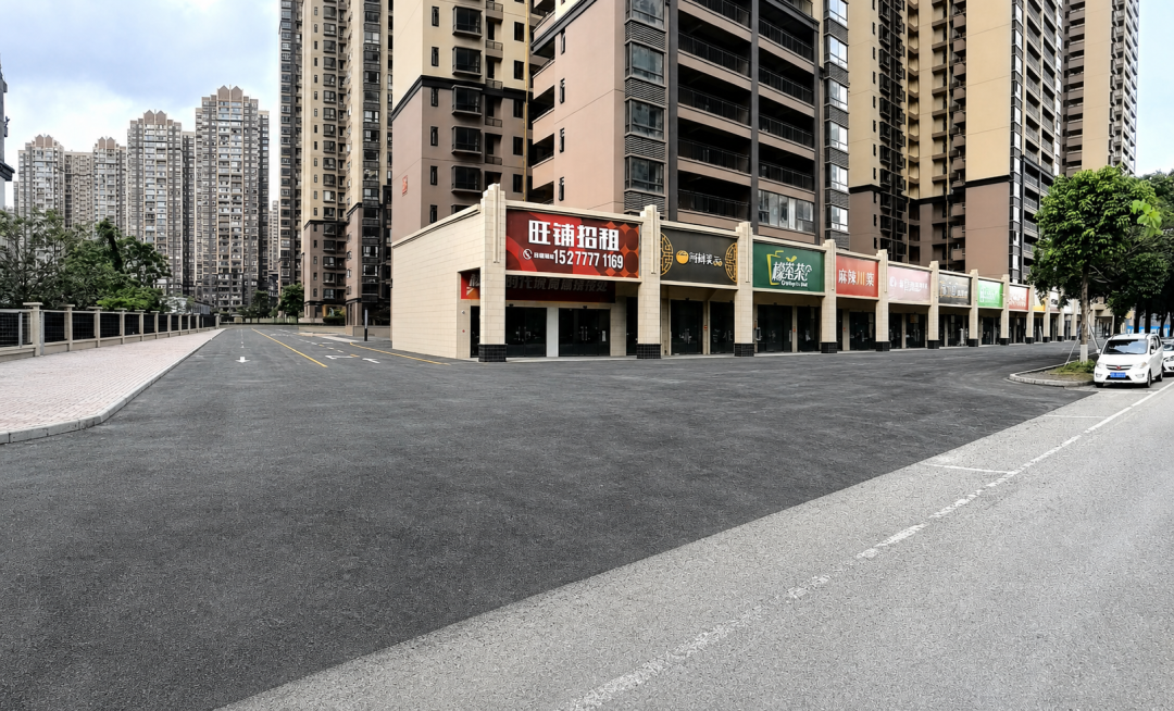 去除图片前景的蓝色围挡、金属围栏和地面障碍物，保留原有商铺、住宅楼、道路和绿植场景，保持整体风格和视角不变，自然衔接修复前景地面预览效果