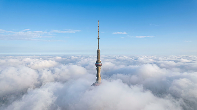 云层之中，平视角度拍摄，东方明珠广播电视塔最顶部的塔尖在云层间若隐若现，背景是晴朗干净的蓝色天空，画质清晰自然，光影柔和