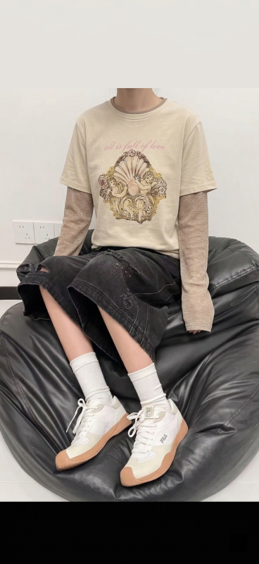 将图片中人物身上的浅绿色条纹开衫替换成图片1中人物所穿的米黄色带天使印花短袖T恤，内搭浅棕色长袖，保持原图片的人物姿态、黑色破洞牛仔裙、白色袜子、白色鞋子、黑色豆袋沙发背景等所有其他内容不变预览效果