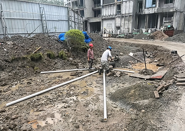 将图中所有弯曲的白色塑料管子修改为笔直状态，保持管子的数量不变，不增加也不减少管子，保持工地场景、人物、泥土、砖块、背景建筑等其他所有元素完全不变，真实摄影风格，自然光影