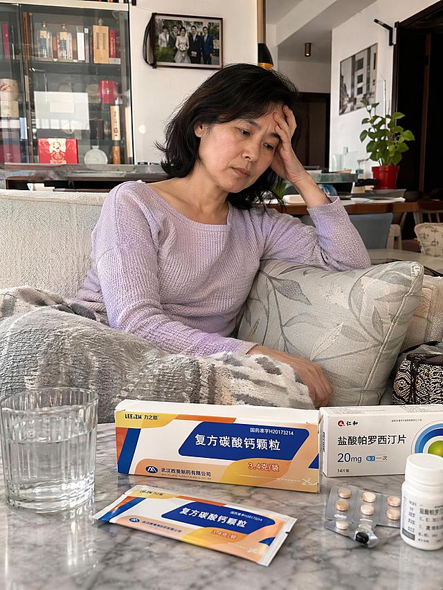 真实生活场景，48岁更年期女性，辞职后在家中客厅沙发休息，桌上放着医生开的这款小袋装复方碳酸钙颗粒产品和其他药物，人物情绪略显疲惫忧郁，居家环境画面丰富真实，写实自然的生活感，产品包装文字清晰可见