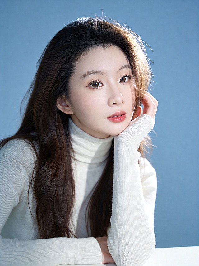 清新温柔风治愈系人像写真,传递纯净松弛的日常氛围感;人物主体:眼神清澈直视镜头(眼神灵动带软萌感,粉橘色唇釉修饰的嘴唇微张),(发丝蓬松有自然空气纹理,右侧发丝轻垂脸颊),清透伪素颜妆(浅棕色眼影自然晕染眼窝,细内眼线放大双眼,底妆轻薄通透保留皮肤原生质感);环境与构图:纯净莫兰迪浅蓝纯色背景,无任何干扰元素,近景取景(覆盖头顶至腰部上方,精准突出面部神态与上半身柔和线条),三分构图(人物面部落在画面左侧1/3与上方1/3交汇点,人物面部为绝对视觉焦点),平拍视角(镜头高度与人物眼部完全平齐,拉近距离增强亲近感);光影与色彩:柔光主光从右侧45°侧方照射,5500K冷白柔光,光线强度柔和不刺眼,发丝边缘形成细腻金边高光,面部光影过渡自然丝滑(柔和阴影轻描下颌线,额头､鼻梁､苹果肌处的高光提亮面部立体感),低饱和度莫兰迪蓝+米白为主色调,低对比度搭配让色彩清新柔和不突兀;细节补充:身着米白色高领针织衫(细腻羊毛肌理清晰可见,修身款式完美贴合身形曲线,高领柔软贴合颈部无紧绷感),动作姿态为右手抬起轻触右侧脸颊,手肘自然支撑在身前平面,身体微侧左肩稍向前,肢体姿态松弛无刻意感;人物居中位于画面中心;氛围与画质:清新柔光氛围滤镜(曝光+3,对比度,8,自然通透感拉满),超高清4K分辨率,中度锐化处理(清晰呈现每一缕发丝纹理､针织衫的细腻肌理以及面部皮肤的通透质感),纯净无噪点,整体画面质感细腻高级,传递出松弛治愈的温柔气质｡