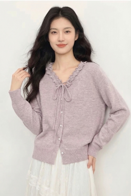 保持模特、淡紫色木耳边系带针织开衫、白色蕾丝半裙、纯白色背景、整体暖柔色调完全不变，仅更换姿势为：一只手轻轻搭在腰侧，另一只手自然抬起触碰发梢，姿态舒展自然，看向镜头，真实感强预览效果