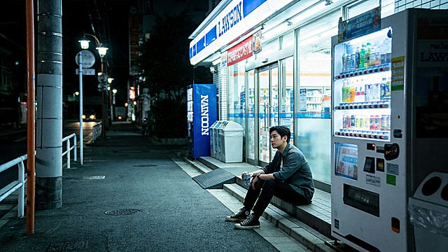 深夜便利店门口场景，一个二十多岁的亚洲男生独自坐在路边台阶上，手里拿着一罐啤酒，便利店的白色灯光和霓虹灯照亮夜晚街道，周围很安静几乎没有人，男生神情有一点疲惫和沉思，城市夜晚空气安静孤独，路边有自动售货机和街灯，冷蓝色夜景与便利店暖白灯光形成对比，真实都市生活感，电影镜头构图，浅景深，高级光影，写实风格，情绪克制，华语情绪歌曲MV画面，电影质感