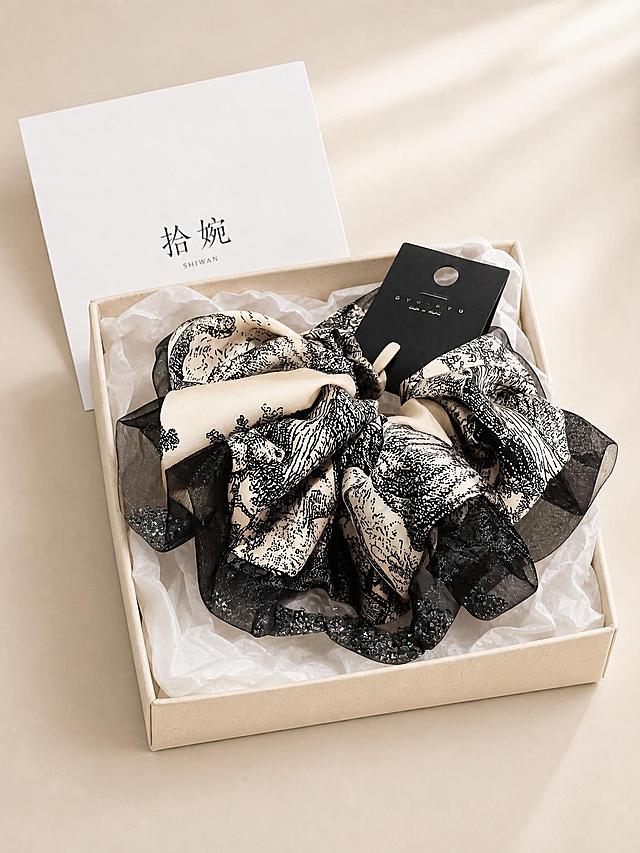 小红书带货图片，产品静物平铺图，俯拍平铺静物摄影，纱边水墨画印花大肠发圈放置在米黄色可降解纸浆盒内，盒内衬白色薄棉纸；盒子后方摆放白色纸质卡片，卡片印有黑色文字"拾婉"；干净浅米色桌面，柔和窗边自然光，韩式简约饰品静物，低饱和莫兰迪色调，高清电商实物实拍，浅景深，面料刺绣纹理清晰细腻，高清，画面简洁高级