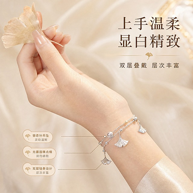 [主图-3] 佩戴效果 手模展示手链上身效果。
[统一基调] 风格=雅致轻奢新中式珠宝商业摄影；背景主色=香槟米杏色绒面质感；标题字色=深棕褐色；辅助字色=暖金色；强调色=暖金；字体=纤细宋体衬线体（标题）+简洁无衬线体（辅助）；组件=细线引线 圆角浅底标签 银杏叶小装饰；光影=柔光箱高光+窄条轮廓光 金属质感细腻。
[画面] 亚洲女性手部特写 手腕自然弯曲 佩戴三生有杏手链 手部占画面约60%；手链双层叠戴效果清晰 银杏叶吊坠垂于手腕内侧 手指轻捏一片干银杏叶；背景为虚化的香槟米杏色丝绸布料 营造温柔氛围。
[光影质感] 珠宝级精修 手链金属光泽与手部肤色协调 皮肤质感自然细腻；侧前方暖柔光 手链在皮肤上有柔和投影 整体光影统一 佩戴效果真实自然。
[配色] 主色香槟米杏 辅色暖金 文字深棕褐 肤色自然通透 背景丝绸质感柔焦。
[文字版式] 画面右上角主标题"上手温柔 显白精致" 下方小字"双层叠戴 层次丰富"；文字右对齐 放在负空间 不遮挡手部和手链主体。
[输出要求] 比例1:1 2048x2048 2K 文字清晰 佩戴自然 产品清晰；负向：变形 错字 手指畸形 面部出现 水印 平台Logo 塑料感 绝对化用语。