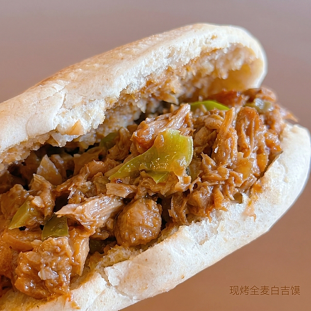 [主图-3] 香卤素夹馍细节特写图
[氛围风格] 美味轻食风，微距食欲感
[画质] 商业摄影质感、光线柔和通透、产品清晰真实、画面干净高级
[元素] 微距特写香卤素夹馍内馅，保持馅料纹理结构颜色与输入产品图绝对一致，清晰展示纤维状植物蛋白素肉碎和青椒块的细节，卤汁油润光泽，颗粒饱满分明，馍皮内侧酥脆纹理也要清晰呈现。商品主体占比75%，特写放大细节，背景浅棕虚化，画面干净简洁
[光影] 自然逆光，打透内馅的油光，形成诱人的光泽轮廓，凸显质感
[配色] 以馅料的酱棕、青椒鲜绿为主，背景浅棕虚化衬托，整体食欲感强烈
[视角构图] 微距特写，内馅充满画面，焦点清晰在馅料纹理上
[文字版式] 右下角标注小字"现烤全麦白吉馍"，浅棕色纤细字体，不遮挡核心特写区域
[比例分辨率] 1:1 比例，2k 分辨率；文字清晰锐利，画面超高清
[负向提示词] 变形，水印，文字错乱，产品图模糊，背景杂乱，颜色失真