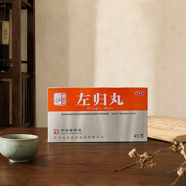 超写实中成药产品场景摄影。
主体：左归丸药盒严格参照上传产品图，完整保留所有可见组件、部件、轮廓、结构、比例、材质、颜色与产品本体上的所有文字信息（logo/品牌名/药品名/规格/批准文号/OTC标识/中华老字号标识等），与上传图完全一致；自然融入场景光影，与场景共处同一物理空间。产品占画面约40%，完整不裁切，背景无其他同类药品包装。
构图：正面平视居中构图，产品位于画面下半部分中央，画面上半部分预留大面积空白区域用于放置文字，留白充足干净。
风格：新中式轻奢高级感。
场景：中式书房桌面场景，温润雅致氛围。
空间/承载：①产品放置于深胡桃木实木桌面上，木纹细腻温润；②背景为米白色宣纸质感背景墙，简洁干净；③画面左侧后方隐约可见深色实木书架一角。
陪衬/软装：①产品左前方，一只小巧的青瓷茶杯，杯中盛有半杯清茶；②产品右后方，一本摊开的线装古籍，书页微黄；③桌面右下角，一小枝干枯的梅花枝桠斜伸而出。
配色/材质：胡桃棕/米白/青瓷青/墨黑；实木/宣纸/青瓷/纸质/干花。
光影：主光从左前方45°斜射，柔和暖调自然光，照亮药盒正面；辅光为右侧环境反射光，阴影柔和自然，整体通透有质感，高级清晰。
参数：4K超写实，细节精致，商业产品摄影质感。严格锁定宽高比为1:1。
