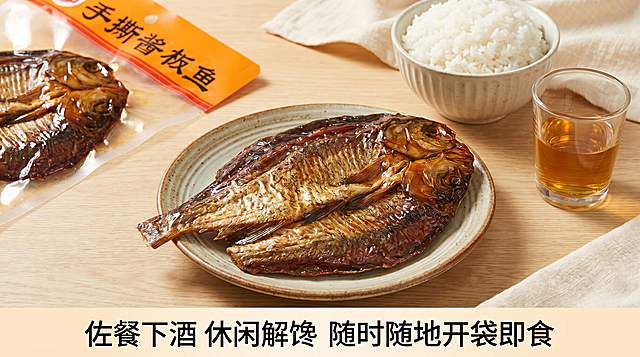 手撕酱板鱼商品详情第三张图，展示食用场景，整份酱板鱼摆在餐盘里，旁边搭配白米饭和酒水，营造解馋下酒下饭的生活场景，左上角露出原包装保持外观一致，商业摄影质感，光线柔和通透，产品清晰真实，画面干净高级，商品主体占比70%，自然暖光氛围，主色调浅米白+深木色，温馨有食欲，平视场景构图，画面底部文案写"佐餐下酒 休闲解馋 随时随地开袋即食"，16:9比例2k分辨率，文字清晰超高清，负向提示词：变形，水印，文字错乱，产品模糊，背景杂乱