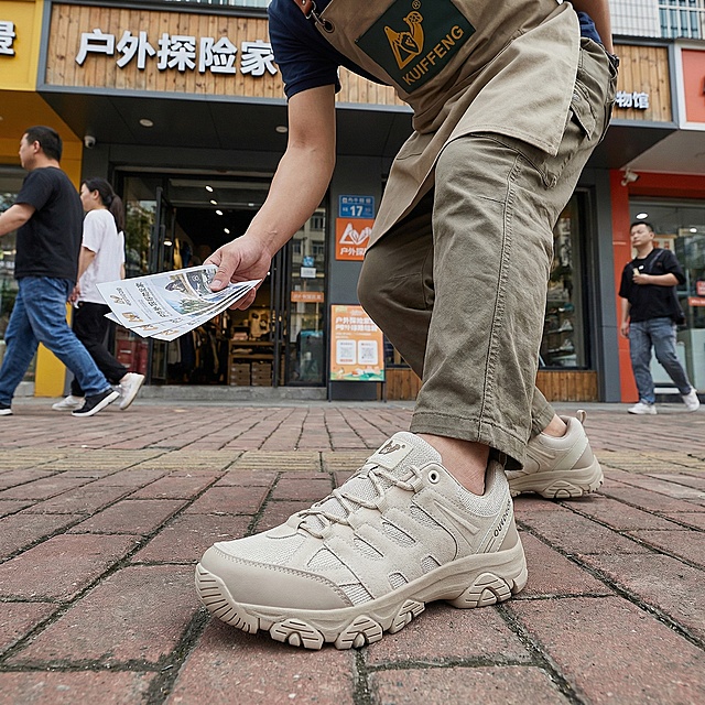 商店门口场景，穿着商店工作服的男子站在门口发传单，脚上穿着这双浅卡其色户外徒步鞋，采用低视角拍摄，画面重点突出脚上的鞋子，鞋子细节清晰，光线自然真实