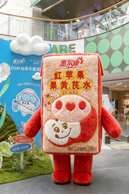 参考图2的惠尔康红苹果黄芪水饮品的外形，以图一的毛绒质感生成同款人形毛绒玩偶，保留饮品瓶身的标签设计和文字，整体为柔软的毛绒材质，摆在商场的活动背景前预览效果