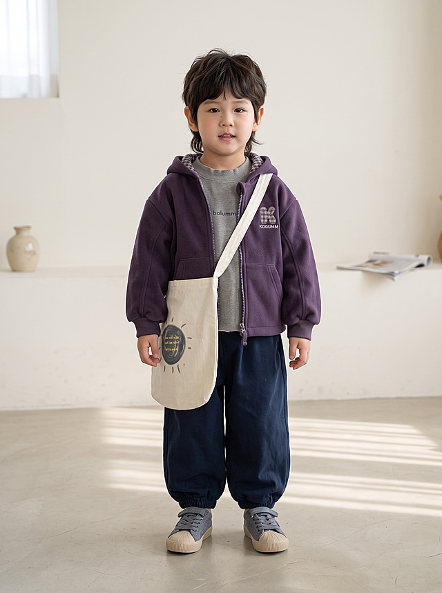 将图片1的儿童紫色连帽外套、藏蓝色裤子和灰色鞋子这套童装穿在图片2的小男孩身上，去掉小男孩原有的蓝色帽子，搭配图片1的米白色帆布包配饰，简约韩系时尚基地背景，全身照，生成自然真实的儿童试穿效果照