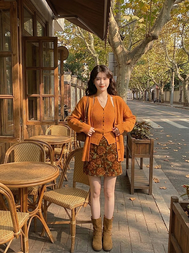 保留这套焦糖秋日穿搭：暖橘色针织开衫+挂脖针织吊带+棕色玫瑰碎花短半裙+棕色短靴，模特改为正面站立整理开衫衣角姿势，复古咖啡馆梧桐露台午后暖金色阳光，凸显服饰，抖音带货风格