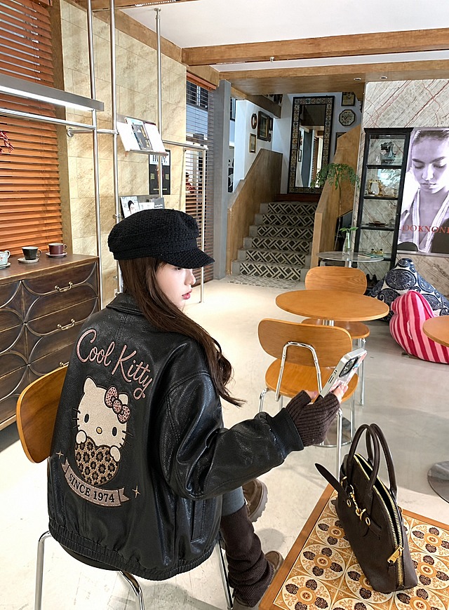 将图3模特身上的黑色皮衣替换为图1和图2所示的Hello Kitty刺绣黑色皮衣，保留模特的五官、脸型、姿势、身体姿态、发型、帽子、手套、靴子完全不变。衣服版型、花色、纹理、面料严格复刻参考服装：黑色皮质翻领夹克，左胸有Hello Kitty贴布绣和"Cool Kitty"刺绣，后背有大号Hello Kitty抱豹纹爱心图案、上方"Cool Kitty"刺绣、下方"SINCE 1974"横幅刺绣及星星装饰，皮质纹理真实，刺绣细节清晰。真实人像摄影，自然光，皮肤质感真实，高清写实，柔和环境光影，衣服贴合身体，服装褶皱自然，无水印，无文字，无logo，无畸形肢体，画面干净，人物长相不变，背景保持原图咖啡馆场景不变。