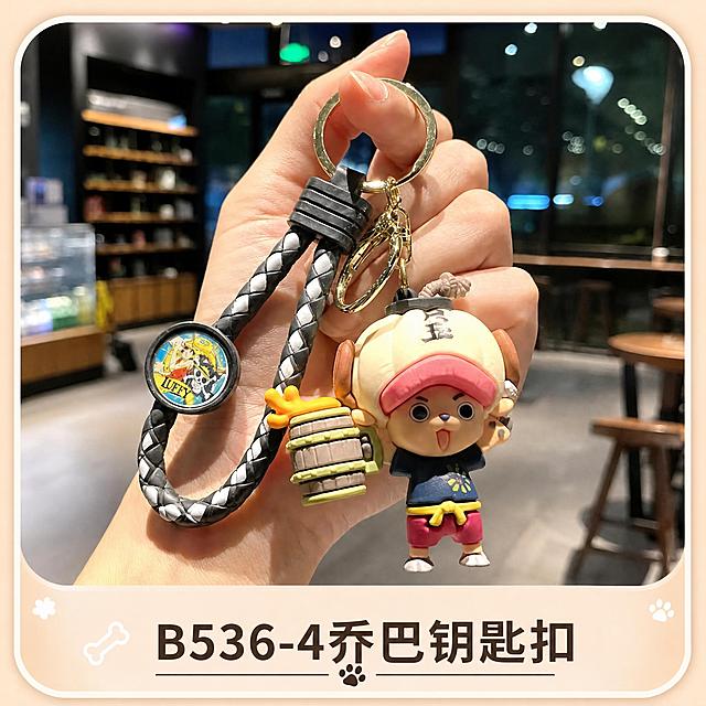 参考第二张图的卡牌设计风格：圆角正方形卡牌，上方是产品实拍图，下方是米黄色底色区域，配有可爱的爪印、骨头装饰元素，底部中间写产品名称文字。现在将第一张图中的乔巴钥匙扣（乔巴公仔，黑灰编织挂绳）作为主体产品图，替换掉原来的索隆款，底部文字改为"B536-4乔巴钥匙扣"，整体布局、装饰元素、风格与参考图保持完全一致，6cm×6cm正方形卡牌，温馨可爱风格