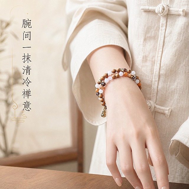 [主图-4] 芭比檀双圈手串手模佩戴展示，呈现腕间佩戴效果与禅意氛围。
[统一基调] 新中式禅意风格，整体色调温润雅致，以米白、浅棕、暖金为主色系；字体采用纤细宋体/书法感衬线体，标题字色深棕近黑，辅助字色暖金；背景自然柔和，光影柔和自然光，全套保持统一的温润质感与留白美学。
[画面] 一只手腕纤细、肤色白皙的东方女性手模，自然垂放在画面中央偏右位置，手腕上佩戴着芭比檀双圈手串。手串双圈环绕在手腕上，松紧度适中，层次分明，底部的金丝玉葫芦吊坠自然垂落在手腕内侧。手模搭配素雅的裸色美甲，手指修长自然。手模身穿新中式盘扣棉麻上衣（米白色或浅卡其色），袖口宽松，露出纤细手腕。背景为柔和的浅米色或虚化的新中式室内场景（如木质桌面、宣纸屏风一角），浅景深突出手腕与手串。
[光影质感] 自然柔和的窗边漫射光线，从左侧45度打下，手腕皮肤呈现细腻白皙质感，手串珠子各材质光泽自然呈现：木珠温润、玛瑙通透、曜石深邃、金丝玉温暖。整体光影柔和不生硬，有真实的皮肤质感与佩戴贴合感。
[配色] 背景浅米白/浅卡其色调，皮肤白皙，手串棕褐、乳白、深咖、橘黄层次丰富，文字深棕+暖金。
[文字版式] 画面左侧或上方留白区域放置文案「腕间一抹清冷禅意」，深棕色纤细宋体，字号适中，竖排或横排雅致排列，可搭配极细的暖金色装饰线条。文字不遮挡手与手串主体。
[输出要求] 1:1比例1440x1440像素，手模自然真实，手串佩戴效果清晰，新中式氛围浓厚；负向：手部畸形、手指多余、手串穿模、颜色偏差、模糊、水印、平台Logo、面部出现、夸张表情。
