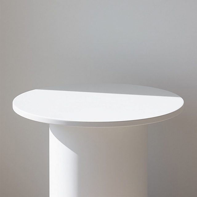 极简风格白色圆形台面，光滑细腻的哑光白色表面，简洁的圆柱形结构，顶部平整边缘圆润，纯白色背景，柔和均匀的自然光从顶部偏左照射，形成轻微的浅灰色投影，整体设计简约干净，无任何多余装饰，突出台面主体的纯粹形态与质感，配色方案极致简单，仅有白色与浅灰色阴影构成。