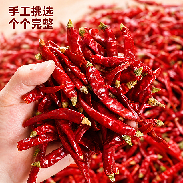 [主图-2] 单手握干红辣椒展示核心品质。[氛围风格] 真实用户视角，直观展示产品品质。[画质] 商业美食摄影质感，光线柔和通透，产品清晰真实，画面干净高级。[元素] 一只手从画面左侧捏起一把干红辣椒，朝向镜头完整展示每根辣椒带新鲜绿色辣椒蒂的形态，背景铺满散落干红辣椒衬托主体。保持干红辣椒外观、完整带蒂形态、物理结构、材质质感、颜色与输入产品图绝对一致，杜绝任何变形和色差，精细化处理。商品主体占比约65%，画面满屏无边框。[光影] 自然室内暖光，顺光打亮手掌和辣椒，辣椒色泽鲜红油亮，背景辣椒柔和虚化，突出主体。[配色] 鲜红辣椒为主，浅肤色手，整体暖调自然配色。[视角构图] 平视特写，中心主体构图，浅景深突出辣椒。[文字版式] 左上左对齐写"手工挑选 个个完整"，深红色粗体，文字放在背景留白处，不遮挡主体辣椒。[比例分辨率] 1:1比例，2k分辨率，文字清晰可辨，超高清。[负向提示词] 变形，水印，文字错乱，产品图模糊，背景杂乱，绝对化用语。