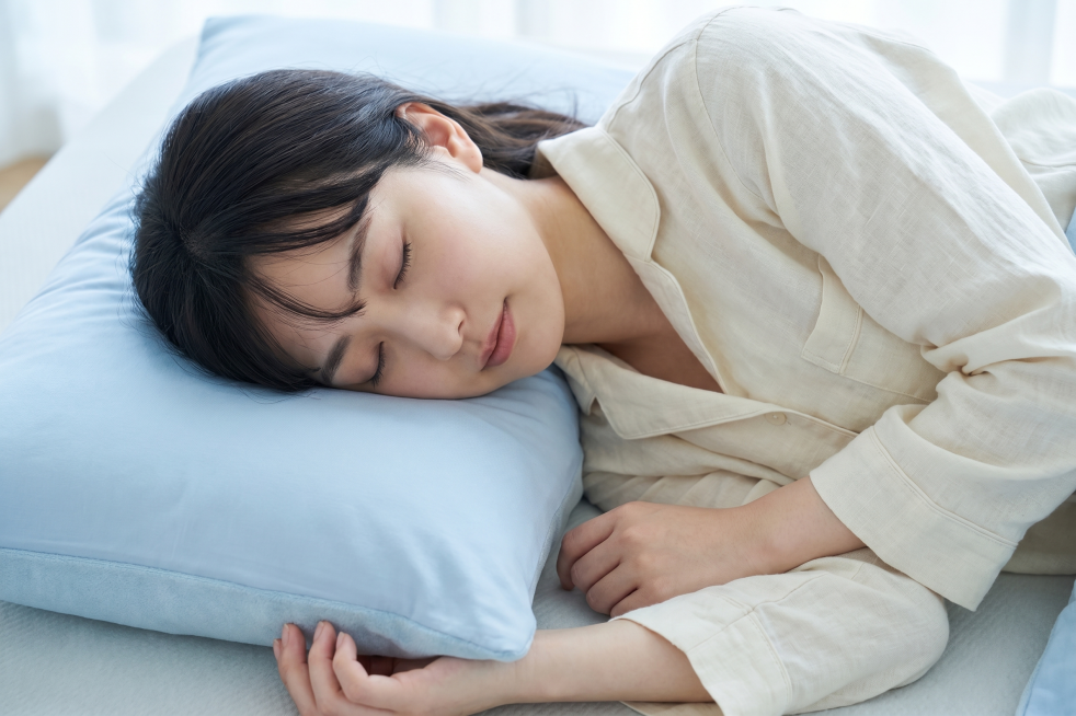 穿着米白色夏季家居服的日本青年女性，躺在床上枕着这款浅蓝色枕头睡得很舒服，第三个不同角度特写商拍照片，给人凉爽舒适的感觉预览效果