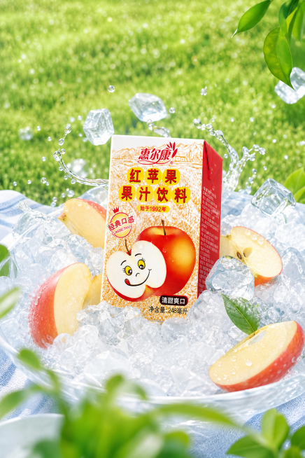 惠尔康红苹果果汁饮料电商海报，保持参考图清爽夏日冰爽户外的风格，将包装盒放在冰块中，搭配新鲜苹果切片，背景为绿色户外草地，构图与参考图不同，突出产品清凉清甜的特点预览效果