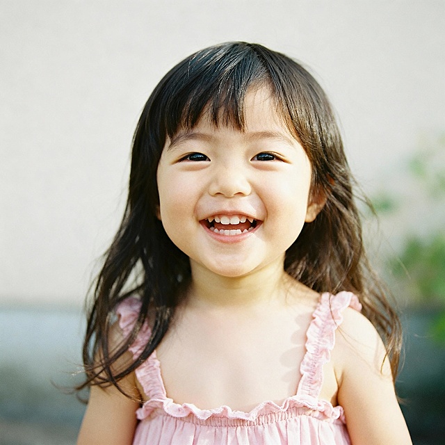 一个3岁左右的小女孩，长发，笑的开心，穿着粉色的小裙子，半身像，皮肤白白的，透着柔嫩感，露出头顶