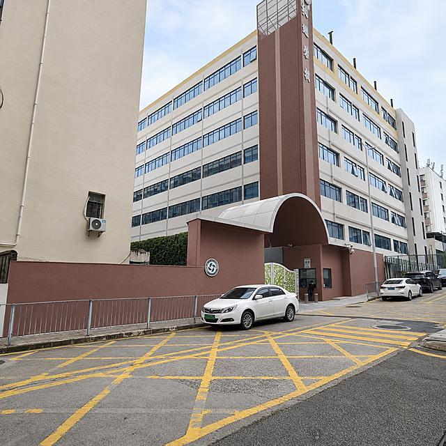 保留原照片的街景构图、透视与地面黄色网格标线，只重新调整建筑与墙面配色：校门竖向塔楼由浓烈酒红改为灰调红棕／深砖赭色，只保留一条竖向色带，相邻墙面与左侧米黄建筑统一为暖米灰；建筑立面的黄色饰条降饱和为浅芥末黄窄线条；拱门与红色矮墙降饱和为灰调红棕；招牌位置保留但不出现文字。整体低饱和、通透、国际化简约，去掉浓烈广告感。画面中不出现任何文字、字母、数字、标语、校名、logo。
