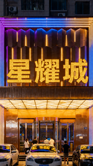 夜晚城市里的商务KTV门头，招牌是巨大的金色发光字体 “星耀城”，门头装饰有暖黄色 + 蓝紫色渐变霓虹灯光，建筑外立面是金属质感的装饰面板，门口停着几辆轿车，有几位顾客进出，整体氛围奢华亮眼，金属质感预览效果