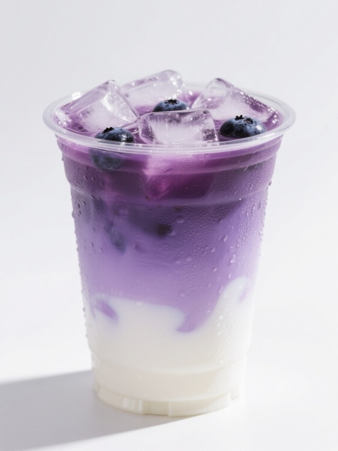 一杯透明塑料杯中装着渐变分层的冰咖啡饮品，顶部覆盖着大量透明冰块，冰块下方是深紫色的蓝莓口味咖啡层，中间过渡为淡紫色，底部是奶白色的奶泡层，整体呈现出清新甜美的蓝莓风味，光线从上方照射，冰块折射出晶莹光泽，杯壁上凝结着细密水珠，背景为纯白色，突出饮品的色彩层次和冰凉质感。预览效果