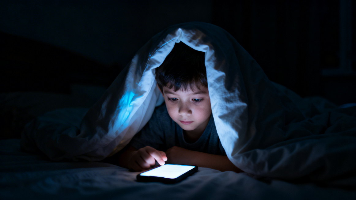 一个小孩在半夜的卧室里，躲在被子下面偷偷玩手机，房间黑暗只有手机屏幕亮着，氛围写实真实，夜晚场景，横版构图预览效果