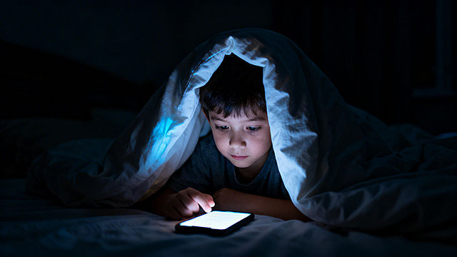 一个小孩在半夜的卧室里，躲在被子下面偷偷玩手机，房间黑暗只有手机屏幕亮着，氛围写实真实，夜晚场景，横版构图