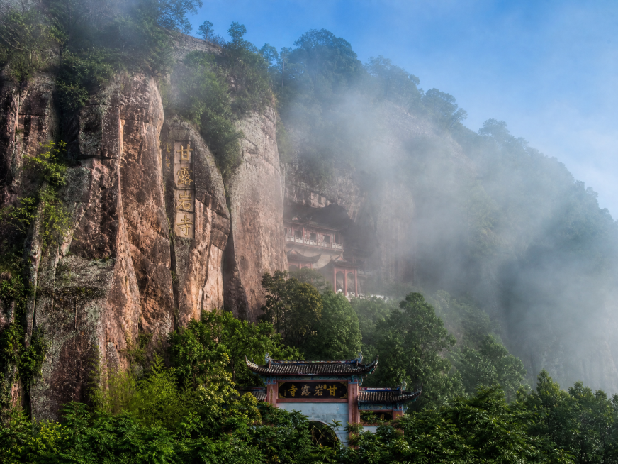 泰宁甘露岩寺外景实拍，清晨雾气缭绕中，千年古刹镶嵌在丹霞岩壁之间，山门隐现于绿树丛中，岩石纹理清晰，古建筑飞檐翘角，远山层叠，自然风光与人文建筑完美融合，写实摄影风格，高清画质，光影自然预览效果