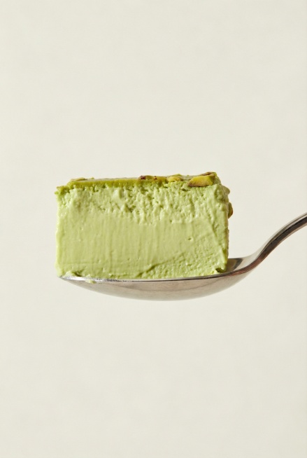 纯侧面视角展示金属勺子，勺子上盛放着一整块开心果味酸奶酪，凝酪质地，其中一面是平整的，色泽呈现自然的开心果淡绿色，质感细腻浓厚预览效果