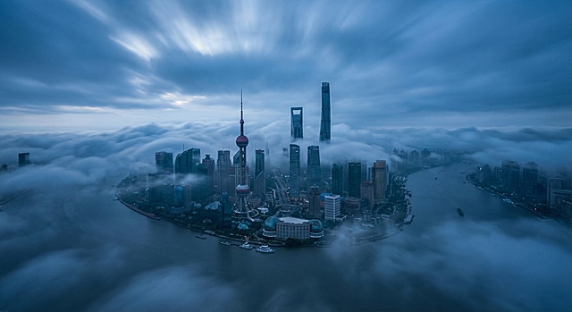 电影级广角航拍，上海陆家嘴与黄浦江的全景俯瞰，摩天大楼群如岛屿般浮现在厚重、阴郁的蓝色云海之上。清晨冷色调，神秘氛围。云雾流动的延时摄影效果。柔和的漫射光，无直射阳光。超写实，8k分辨率，孤独与宏大感