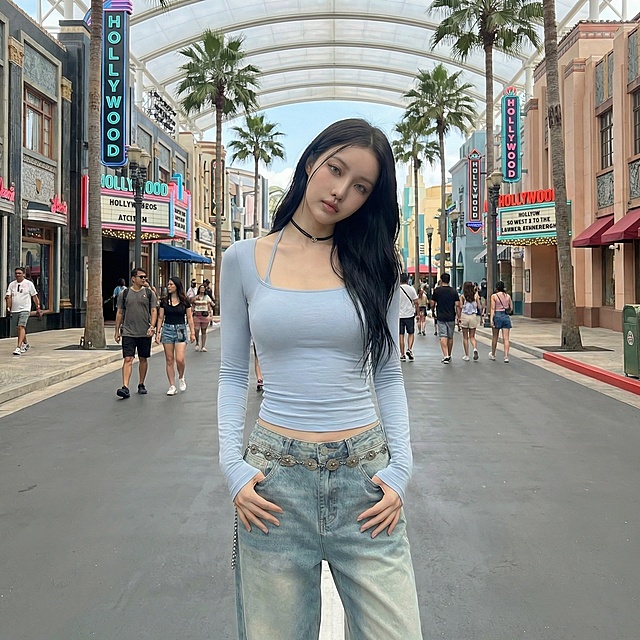 将背景替换为环球影城内部场景，保持模特和服饰不变，更换为双手插兜歪头的姿势