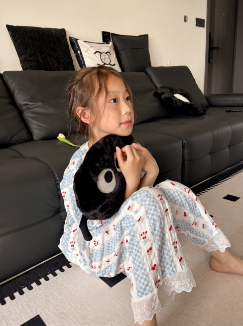 [主图 3] 儿童家居服模特坐姿展示图，保留原模特和蓝白红樱桃图案家居服，延续首图温馨暖调居家场景风格。[氛围风格] 温馨自然松弛居家氛围；[画质] 商业摄影质感、光线柔和通透、产品清晰真实、画面干净预览效果