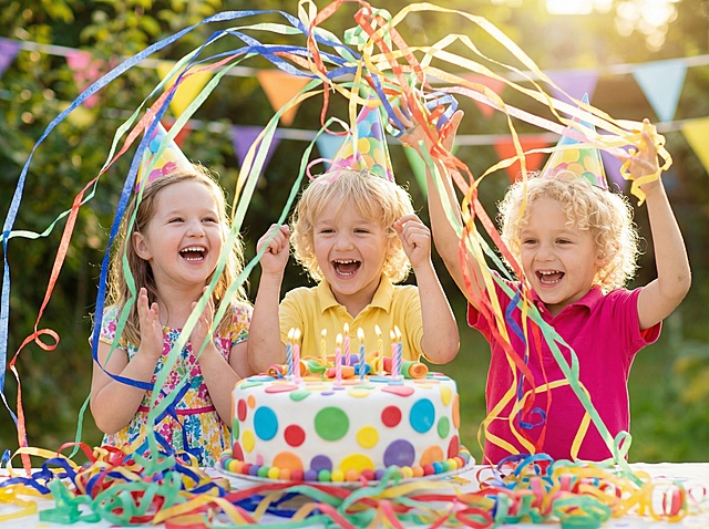 生成一张儿童生日场景图，三个外国儿童围在生日蛋糕周围，前景是参考图的纸质彩带向空中抛开，有些长长的彩带在空中散开，还有些彩带在孩子们的前面，画面营造一种开心的氛围