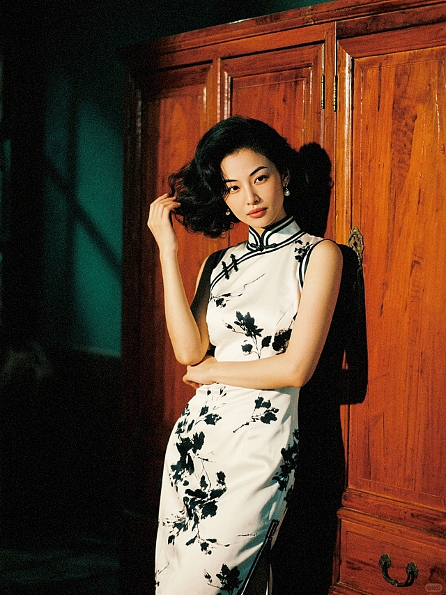 夜晚，一个女生（穿白底黑色水墨印花旗袍，手推波发型）倚在老式红木衣柜前，韵味十足的抚摸头发。