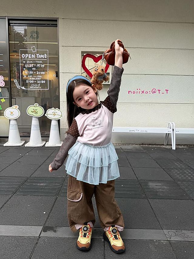 将图中儿童脚上的鞋子替换为参考图中的黄黑棕拼色旋转纽扣儿童运动鞋，旋转纽扣上的图案为TOM字样，鞋子款式、颜色、细节与参考图完全一致，人物、服装、背景、姿势、光线、构图均保持不变，自然贴合脚部角度和透视关系