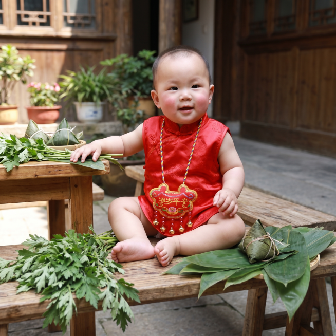 1岁左右中国宝宝脖子佩戴岁岁平安刺绣香包挂脖，端午节日庭院场景，绿色粽叶点缀，温馨自然真实宝宝照片预览效果